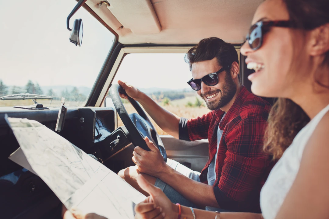 Couple souriant dans un VR vintage, en train de lire une carte routière pendant un road trip en Gaspésie par temps ensoleillé.